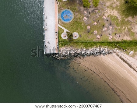 An aerial view over a waterfront park with a beach in Brooklyn, New York on a sunny day with clouds. Taken by a drone camera.