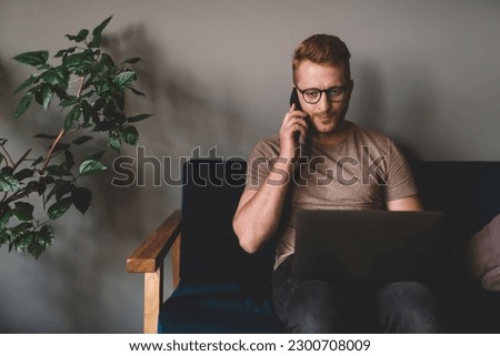Caucasian freelance copywriter reading received online messages on modern laptop computer while making consultancy mobile conversation,skilled man in optical spectacles browsing web pages and calling