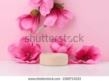 Empty round wooden platform and branches with pink magnolia flowers on a pink background. Place for demonstration of products, cosmetics