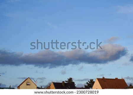 Picturesque view of the roofs of private houses and blue sky with a cloud.