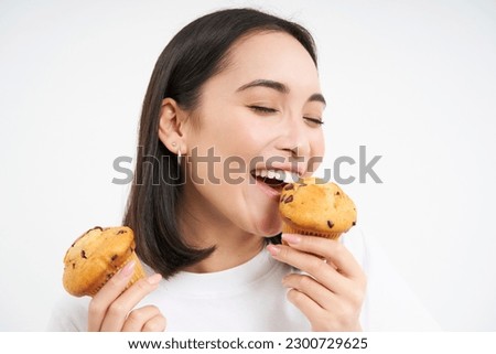 Close up portrait of asian girl eats cupcakes with happy face, isolated on white background.