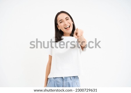 Enthusiastic asian woman, points finger at camera, congratulating, peeking you, inviting people, isolated on white background.