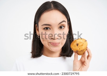 Image of young asian woman, nutritionist showing pastry cupcake with lots of calories, forbid eating junk food, white background.