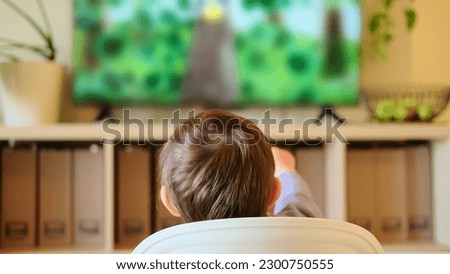 Toddler baby is having fun watching TV while sitting on the high chair. A little child watching a cartoon on the television set with happiness Kid aged about two years (one year ten months) Royalty-Free Stock Photo #2300750555