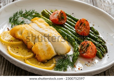 Fried halibut loin with cooked green asparagus and tomatoes on wooden table 
