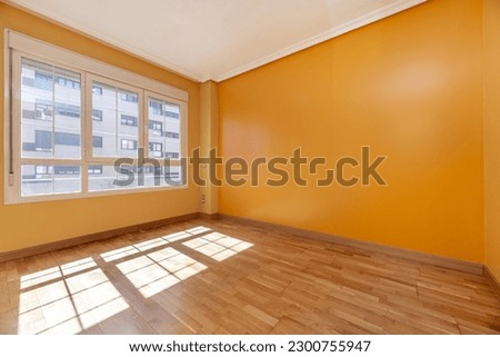 Empty room with oak floors, a large window through which the sun streams in