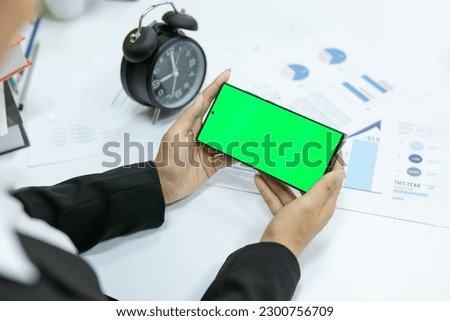 woman use green screen smartphone in office.back view of asian woman take green screen smartphone.Asian businesswoman show green screen of mobile confidently in the office