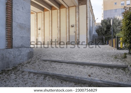 An urban corner with sand on the floor under the walls of a bridge and a small playground