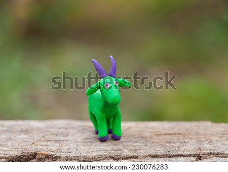 Plasticine world - little homemade green goat with purple horns stand on a wooden floor, selective focus and place for text