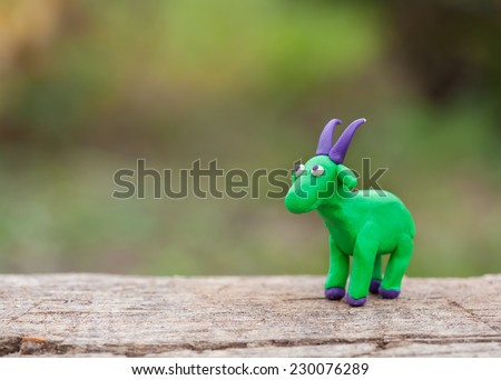 Plasticine world - little homemade green goat with purple horns stand on a wooden floor, selective focus and place for text