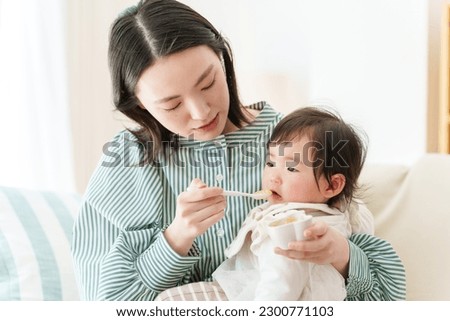 young asian mother feeding baby food to her baby in living room Royalty-Free Stock Photo #2300771103