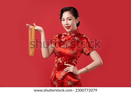 Chinese new year festival, Beautiful Young asian woman wearing traditional cheongsam qipao dress with gold necklaces on red background, Royalty-Free Stock Photo #2300772079