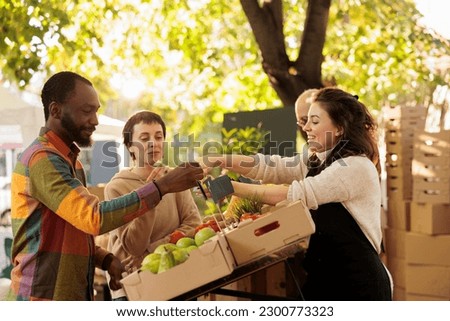Vendor offering samples to customers while selling home-grown fruits and vegetables at local farmers market. Young multiracial family couple tasting natural organic produce while visiting food fair Royalty-Free Stock Photo #2300773323