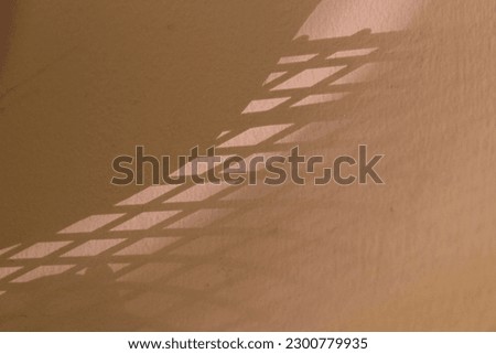 An abstract shadow of a grid on a peach-colored wall in a house