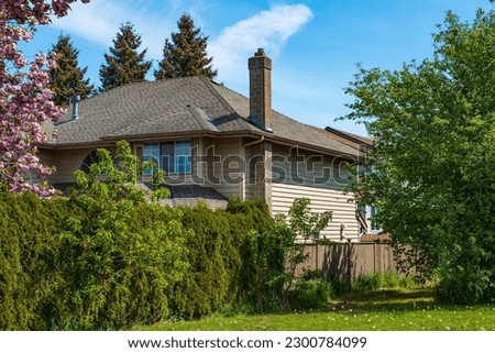 Real Estate Exterior Front House with beautiful garden on a sunny day. Big custom made house with back yard, fence and green lawn in the suburbs in Canada in springtime. Street photo, nobody