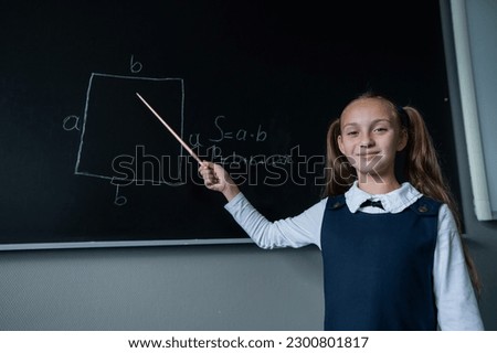 The schoolgirl answers at the lesson. Caucasian girl writes a formula on a blackboard.