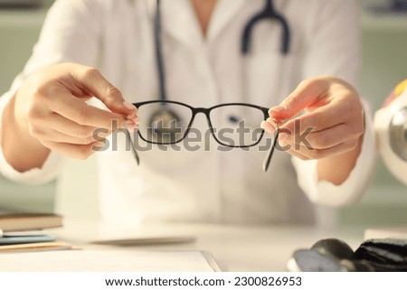 Close-up of woman doctor giving pair of black glasses to patient. Eyesight test and correction excellent vision, laser surgery, alternative driver health certificate or examination concept Royalty-Free Stock Photo #2300826953