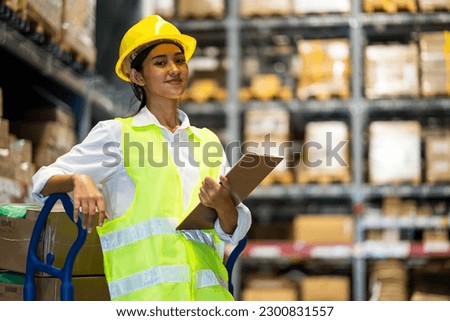Young smiling woman worker and vest checking box in stock in factory warehouse, Staff check stock girl prepares shipping goods and packaging products to customer. Royalty-Free Stock Photo #2300831557