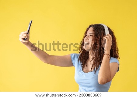 Young woman taking a picture with her white headphones on a yellow background.