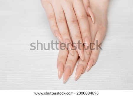 Elegant pastel pink natural manicure. Female hands  on white wooden background.