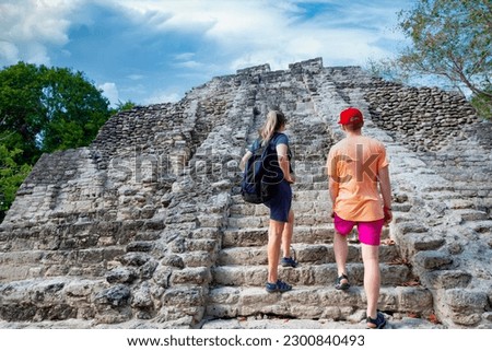 Two Adult Tourists climbing the stairway of large Mayan temple ruins while on vacation. View from behind with large stone steps leading up to the top of the Mayan Temple Royalty-Free Stock Photo #2300840493