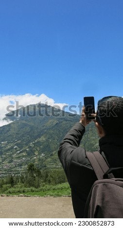 a young traveller man taking portrait picture of beautiful mountain and sky scenery view using his smartphone. healthy lifestyle outdoor activity.