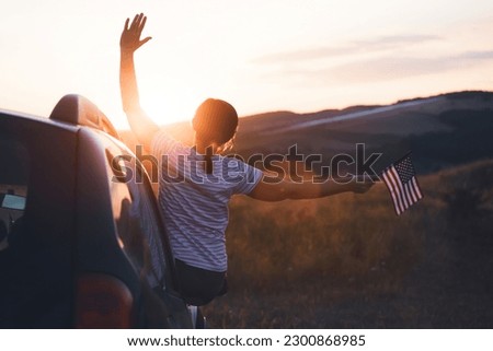 Woman holding an American flag on a road trip. Independence Day or traveling in America concept.