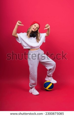 A teenager girl holds volleyball ball in hand and smiles on a red yellow background. Studio photo.