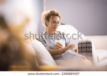 Modern lady having relax at home sitting on couch and using ereader tablet to read an online ebook. Woman using technology indoor leisure activity alone enjoying relaxation on couch. Indoor life Royalty-Free Stock Photo #2300889407