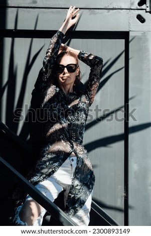 woman in sunglasses stands in the shade against a dark wall