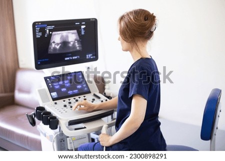 Doctor woman in uniform sitting in office in hospital with ultrasound diagnostic machine equipment and ready to examine patients doing ultrasound of thyroid gland. Ultrasound scanning diagnostic Royalty-Free Stock Photo #2300898291