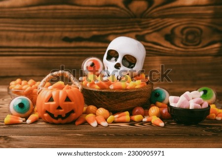 Halloween pumpkin-flavored corn candy, jelly eye, sugar skull and jelly beans on a brown background. Classic sweet Halloween treats. Halloween holiday concept and Jack lantern.Place for text. 