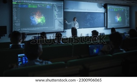 Young Female Teacher Giving a Data Science Lecture to Diverse Multiethnic Group of Female and Male Students in Dark College Room. Projecting Slideshow with Neural Network Model Royalty-Free Stock Photo #2300906065