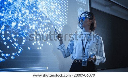 Young University Professor Explaining a Web Development Project to a Group of Students in a Dark Auditorium. Female Teacher Showing a Back-End Programmers Code on a Big Projector Screen Royalty-Free Stock Photo #2300906079