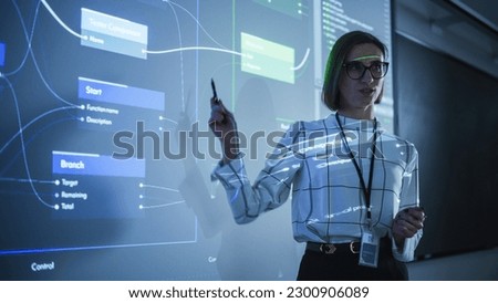 Portrait of a Young Female Professor Explaining Big Data and Artificial Intelligence Research Project in a Dark Room with a Screen Showing a Neural Network Model. Computer Science Education in College Royalty-Free Stock Photo #2300906089