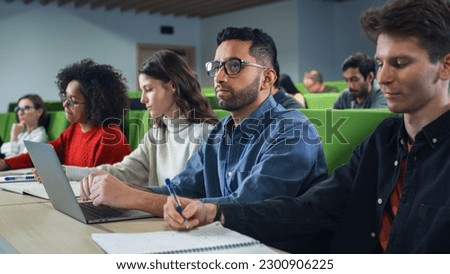 Smart Handsome Male Student Studying in University with Diverse Multiethnic Classmates. Young Man is Using a Laptop Computer to Summarize the Lecture, Study at Home and Pass the Exams Royalty-Free Stock Photo #2300906225