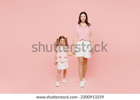 Full body smiling woman wear casual clothes with child kid girl 6-7 years old. Mother daughter look camera hold hands walk together isolated on plain pastel pink background. Family parent day concept