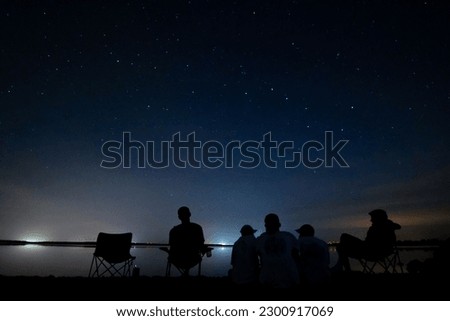 A group of people sitting on the coast of river with starry sky at night in the background