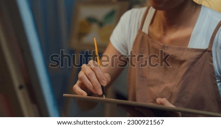 Close-up Youth Asia lady wear apron holding palette use brush painting on canvas create artwork cozy workshop in home at night. Contemporary Painter Abstract Modern Art, Creativity and people concept.