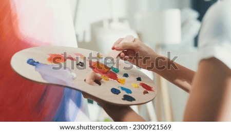 Close-up youth Asia lady wear apron holding palette color use brush painting on canvas create artwork in cozy workshop at home. Contemporary Painter Abstract Modern Art, Creativity and people concept.