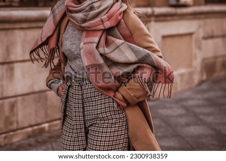 Woman in autumn stylish fashion brown long coat, scarf and plaid pants walking in the city. Female casual street style outfit. Film grain effect Royalty-Free Stock Photo #2300938359