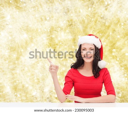 christmas, winter, holidays, happiness and people concept - smiling woman in santa helper hat pointing finger over yellow lights background