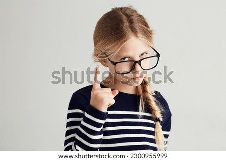 Strict, serious and portrait of a child with a gesture isolated on a white background in a studio. Rude, smart and a young girl wearing glasses and gesturing with finger for discipline on a backdrop Royalty-Free Stock Photo #2300955999