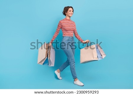 Full length photo of adorable sweet lady wear pink shirt walking holding shopping packages isolated blue color background