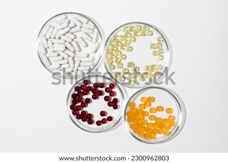 Four laboratory petri dishes with pills capsules in yellow, white, red and orange colors on a white isolated background.