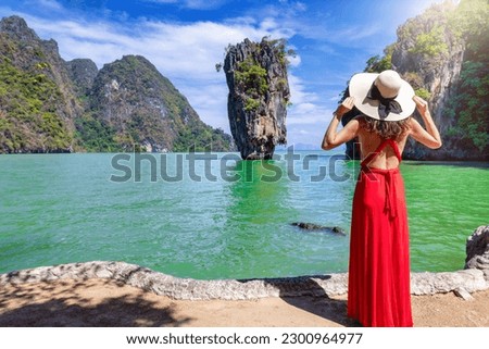 A tourist woman in a red dress looks at the famous sightseeing spot James Bond island at Phang Nga Bay, Phuket, Thailand Royalty-Free Stock Photo #2300964977