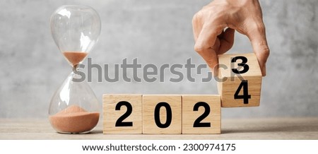 hand flipping block 2023 to 2024 text with hourglass on table. Resolution, time, plan, goal, motivation, reboot, countdown  and New Year holiday concepts Royalty-Free Stock Photo #2300974175