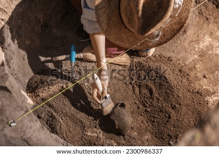 Female archaeologist digging up ancient pottery object at an archaeological site. Royalty-Free Stock Photo #2300986337
