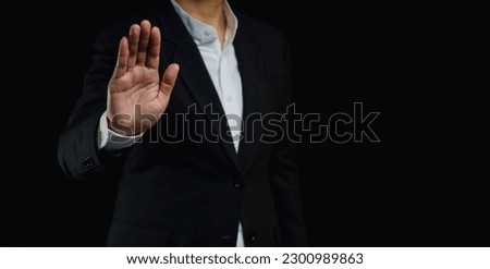 A businessman in a suit shows a stop gesture while standing on a black background. Space for text. Close-up photo
