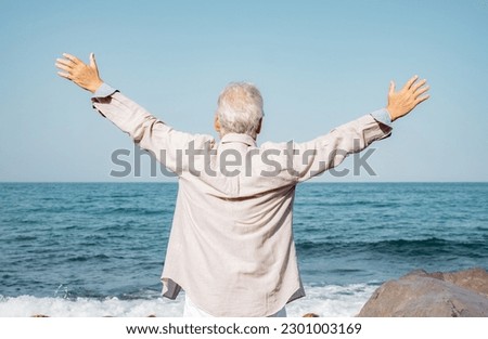 Vacation Retirement Lifestyle concept at Sea, Back View of Happy Senior Man with Outstretched Arms Relaxing at the Beach - Stilish Elderly Grandfather Enjoying Freedom Royalty-Free Stock Photo #2301003169